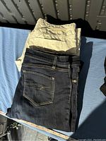 Two pairs of women's size 12 pants, one dark denim and one white skinny crop, folded and laid flat.