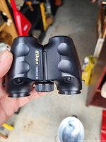 Close-up photo of Nikon Travelite II binoculars held by hand showing brand name and model with textured grips and central focus knob.