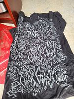 Front of black T-shirt showing graffiti-style white text graphics covering most of the shirt surface.