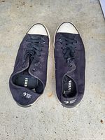 Top view of the pair of black Converse sneakers placed toe-to-toe on a concrete surface, showing wear and visible use marks.