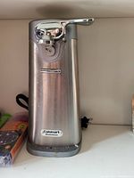 Front view of a tall Cuisinart stainless steel electric can opener showing the handle, cutting mechanism, and power cord.