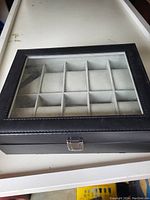 Closed black jewelry case with glass lid showing divided compartments inside