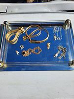 Photo of assorted jewelry on a glass tray showing two bracelets, multiple pairs of earrings, and two necklaces.