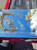 Assorted gold-tone and silver-tone necklaces and chains on glass tray, displayed in natural light.