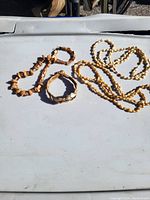 Photo showing three bamboo style gold-tone jewelry pieces laid out on a white surface in sunlight.