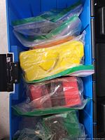 Multiple blocks of clay in various colors contained in ziplock bags inside a blue storage box. Colors include yellow, red, green, orange.