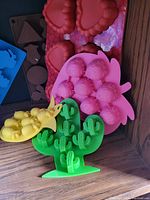 Multiple silicone molds including green cactus, pink strawberries, and yellow pineapples visible with red hearts in background.