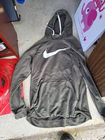 Full view of olive green Nike hoodie sweatshirt with white swoosh logo and front pouch pocket on concrete floor.