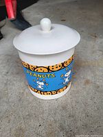 Side view of the white glass container with blue Peanuts-themed decoration and white lid with round knob.