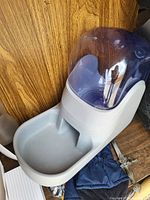 Photo of automatic pet feeder with clear plastic food container and grey plastic food tray taken on wood surface