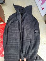 Photo of folded outer shell of black and grey checkered Point Zero coat showing collar and sleeve patch