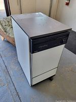 Front-facing photo of a white portable washing machine with a black control panel at top.