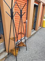 Two standing coat racks with black metal frames and triangular wooden shelves, positioned outdoors near orange storage unit doors