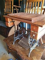 Full view of antique sewing machine cabinet showing wood top, drawers, and wrought iron foot pedal base with Raymond name.