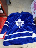 Front view of a royal blue Toronto Maple Leafs hockey jersey with white stripes and the team logo on the chest.