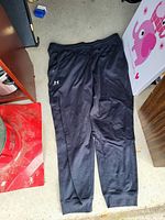 Full view of black Under Armour jogger pants laid flat showing style, logo, and fit