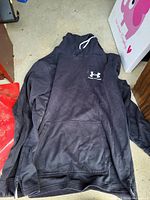 Full view of black Under Armour hoodie sweater with front pocket and logo on chest.