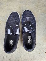 Top view of Vans slip-on shoes showing black and grey patterned upper with elastic side accents and Vans logo on the insole.