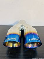 Front view of dual stainless steel exhaust tip with blue burn gradient and NETAMI branding at outlets