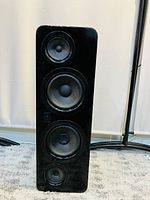 Full view of one black floor standing speaker showing four visible speaker drivers.