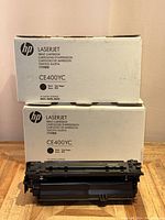 Two HP CE400YC black toner cartridge boxes stacked with one cartridge in front showing the black toner drum.