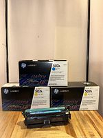 Photo showing three HP 507A toner cartridge boxes with one cyan toner cartridge displayed in front.