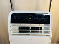 Front view of the white Insignia portable air conditioner showing the black control panel with digital display and function buttons, and adjustable front louvers.