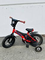 Side view of red Trek kids bike with black training wheels, black fenders, and beige handle grips, showing overall bike condition and design.