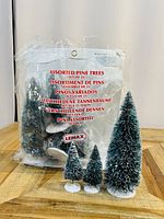 Set of 21 miniature faux pine trees of varying heights in a plastic bag, with printed label showing brand Lemax and multiple languages.