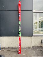 Full-length view of one red Atomic Powerflex Salmon ski upright on concrete floor against dark wall