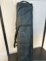 Black fabric carrying bag for roll up banner stand, shown upright with zipper and shoulder strap.