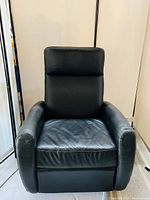 Front view of a contemporary black leather recliner with padded armrests and high backrest.