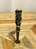 Front view of brass nutcracker depicting Fagin character standing on wooden parquet background.