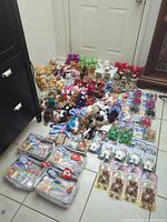 Wide view of over 100 Ty Beanie Babies plush toys arranged on floor, showing variety of animals and colors, including multiple duplicates towards back and sides.