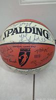 Full view of signed Spalding WNBA official game ball showing multiple player signatures on white and orange panels.