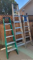 Three ladders standing side by side outdoors, two green Werner 6 ft ladders and one blue Keller 8 ft ladder