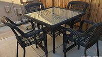 Full view of the glass-top wicker outdoor table with four chairs surrounding it on patio.