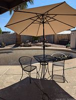 Full view of bistro set with umbrella opened, showing two chairs, square table, and beige umbrella casting shadow on the concrete patio.
