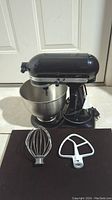 Front view of black KitchenAid Classic tilt-head stand mixer with stainless steel bowl and two attachments in front.