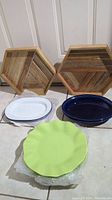 Two wooden Nate Berkus coffee trays with chevron wood pattern, two oval serving platters with white and blue finish, one green Crate and Barrel ruffled platter, and one blue Fiesta platter.