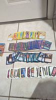 Mixed trading cards including Pokemon, Yu-Gi-Oh, Magic The Gathering, and Wacky Packages cards laid out on floor tiles.