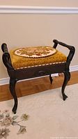Front and side view of antique dark wood stool with floral needlepoint cushion and carved legs on a beige carpet.