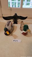 Three bird figurines: two wooden mallard ducks painted with natural colors and a black soapstone bird with wings open, displayed on a table.