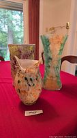 Three decorative glass vases displayed together on a red cloth: tall green-beige vase, mottled purple-green vase, and smaller owl-shaped vase.