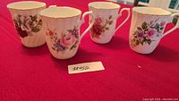 Four Royal Sutherland fine bone china mugs displayed on a red cloth, showing floral designs and gold rims.