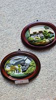 Two hand painted 3D sculptured oval frames lying on a textured carpet surface showing the scenery and frames from a distance.