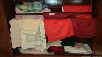 Shelf with assorted folded tablecloths, placemats, and napkins in colors including red, burgundy, white, green, and pink