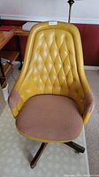 Front view of the vintage yellow vinyl office chair showing button tufted backrest and brown fabric seat cushion.