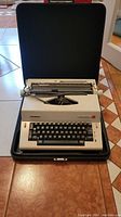Olympia electric typewriter inside its black carrying case, showing keyboard and overall machine.