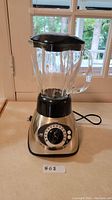 Full view of Oster blender showcasing glass jar, black lid and stainless steel base with control knob.